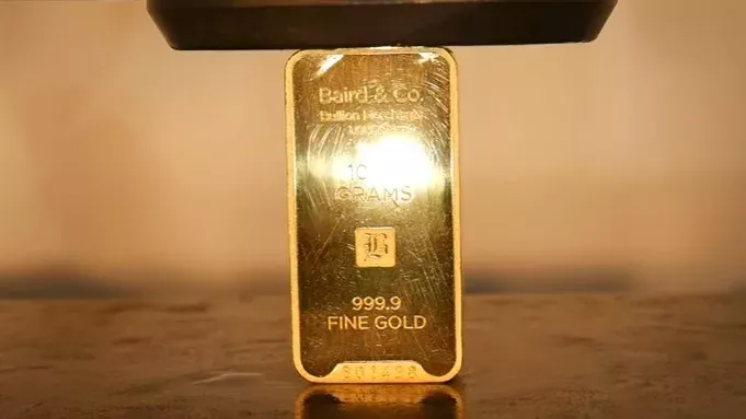 Ein Mann zerquetscht einen Goldbarren mit einer hydraulischen Presse