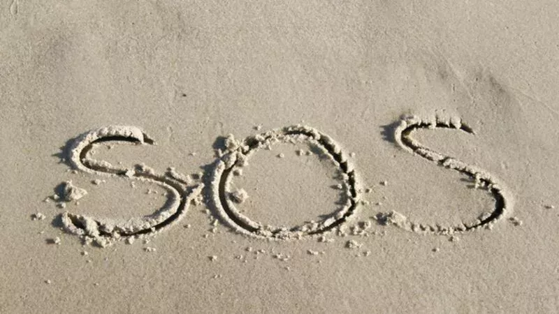 Gestrandet auf einer einsamen Insel rettet ihnen ein SOS im Sand das Leben