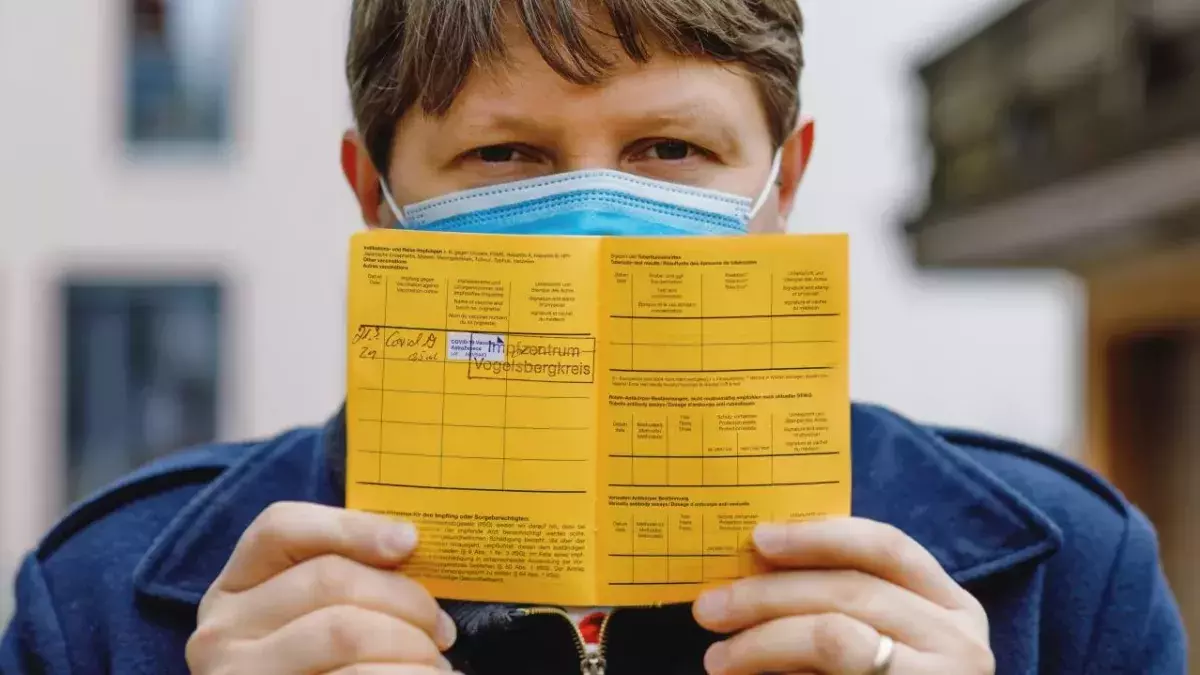 Ein Mann mit Mund-Nasen-Schutz hält einen gelben Impfpass in den Händen