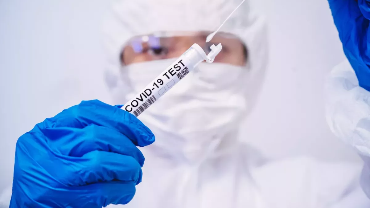 Ein Mediziner mit Schutzkleidung hält einen Corona-Test in den Händen