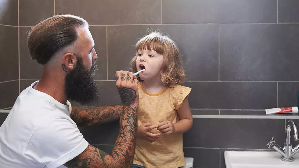 Tätowierter Vater putzt seiner Tochter die Zähne