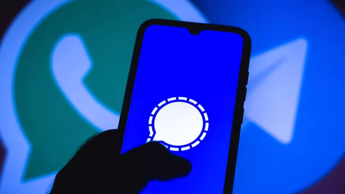 Das Signal-Logo ist auf einem Handy-Bildschirm abgebildet, mit dem Whatsapp und Telegram-Logo im Hintergrund