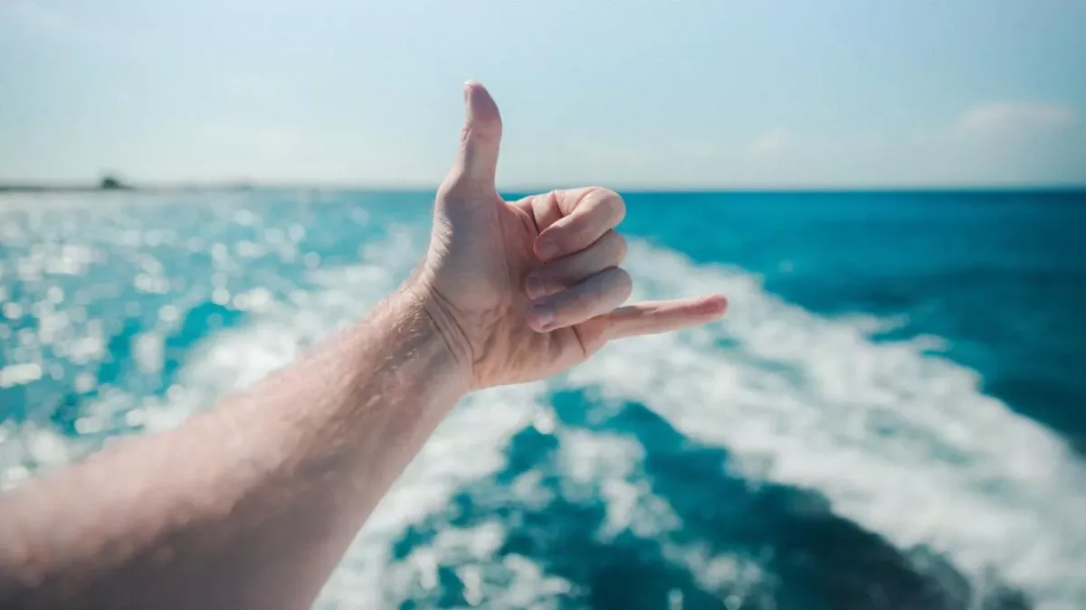 Ein Mann macht den Shaka-Gruß mit seiner linken Hand auf dem Ozean