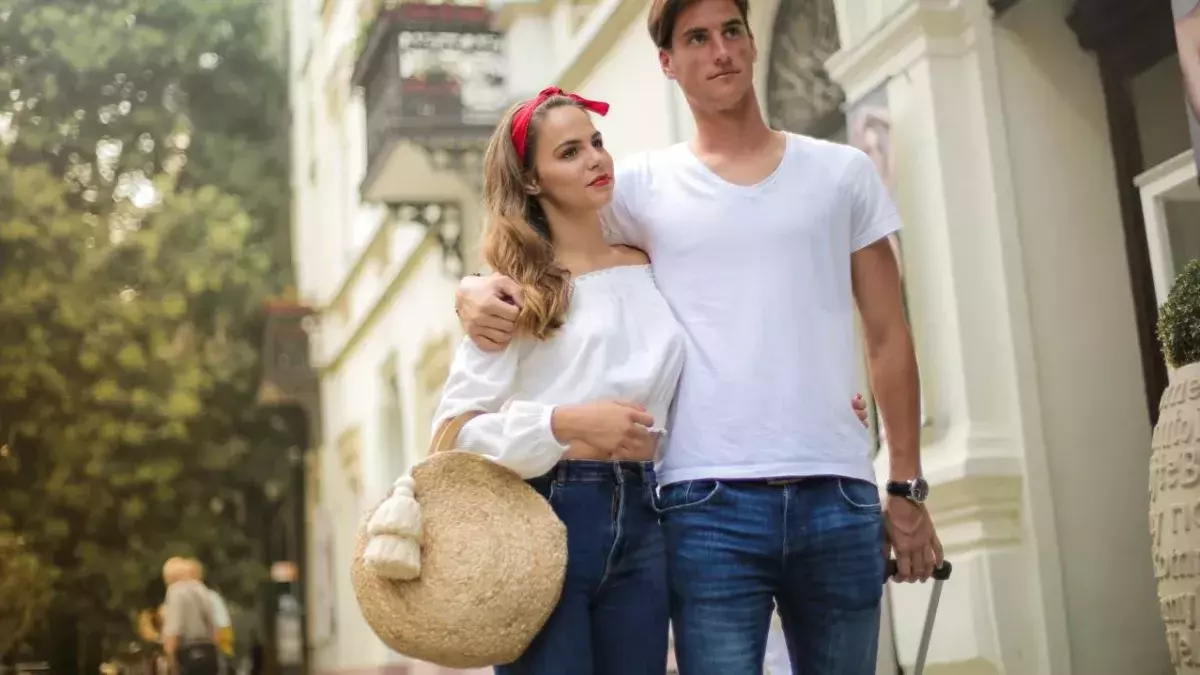 Ein Paar läuft Arm in Arm mit Koffer und Korbtasche durch eine Stadt