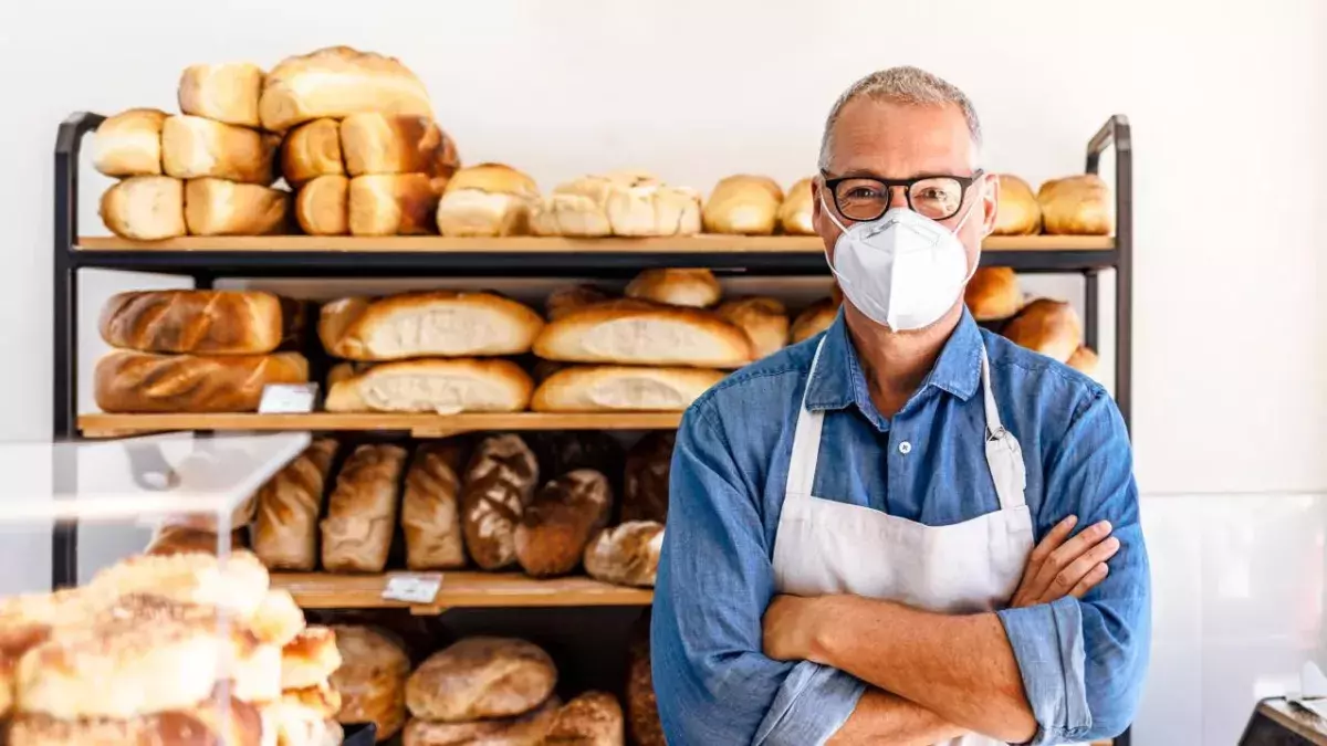 Mann, der in einer Bäckerei arbeitet und eine Gesichtsmaske trägt, um das Corona-Virus zu vermeiden