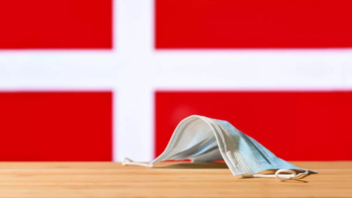 Eine medizinische Maske liegt auf dem Tisch vor dem Hintergrund der Flagge von Dänemark
