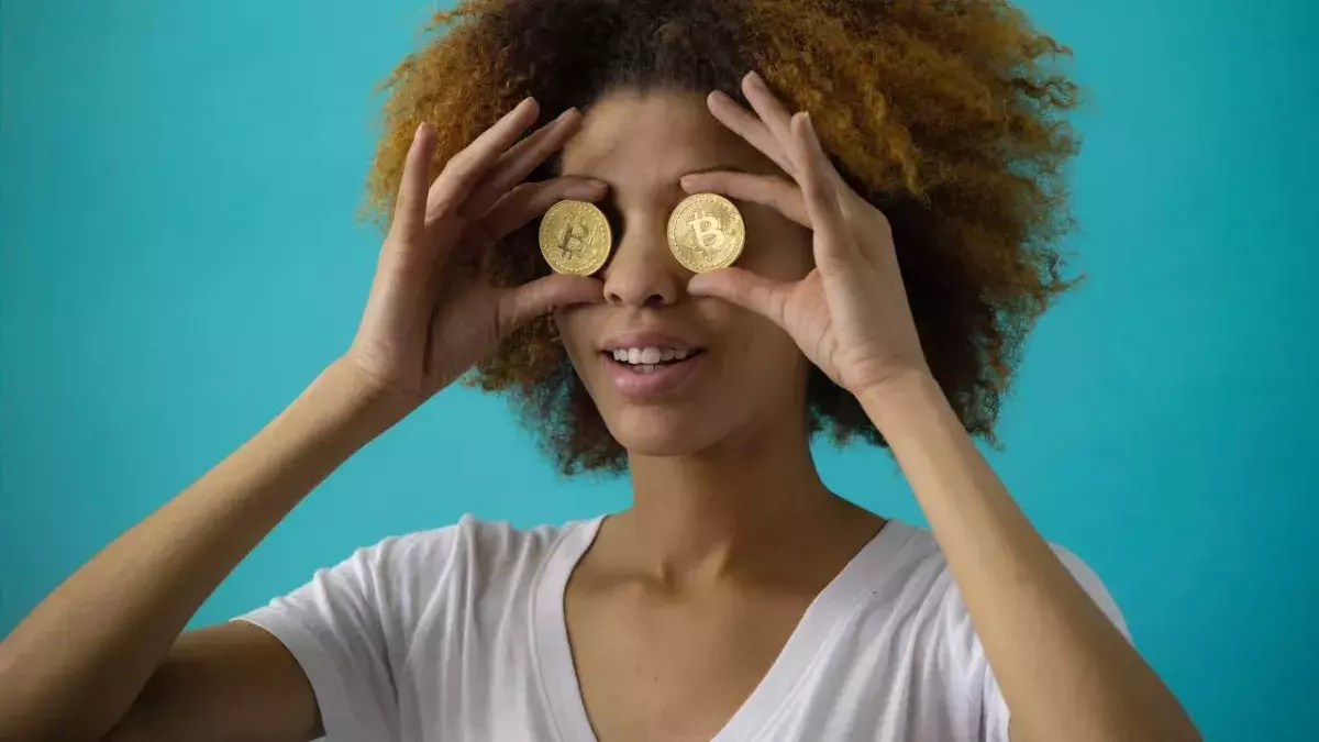 Eine Frau hält sich zwei Bitcoin-Münzen vor die Augen