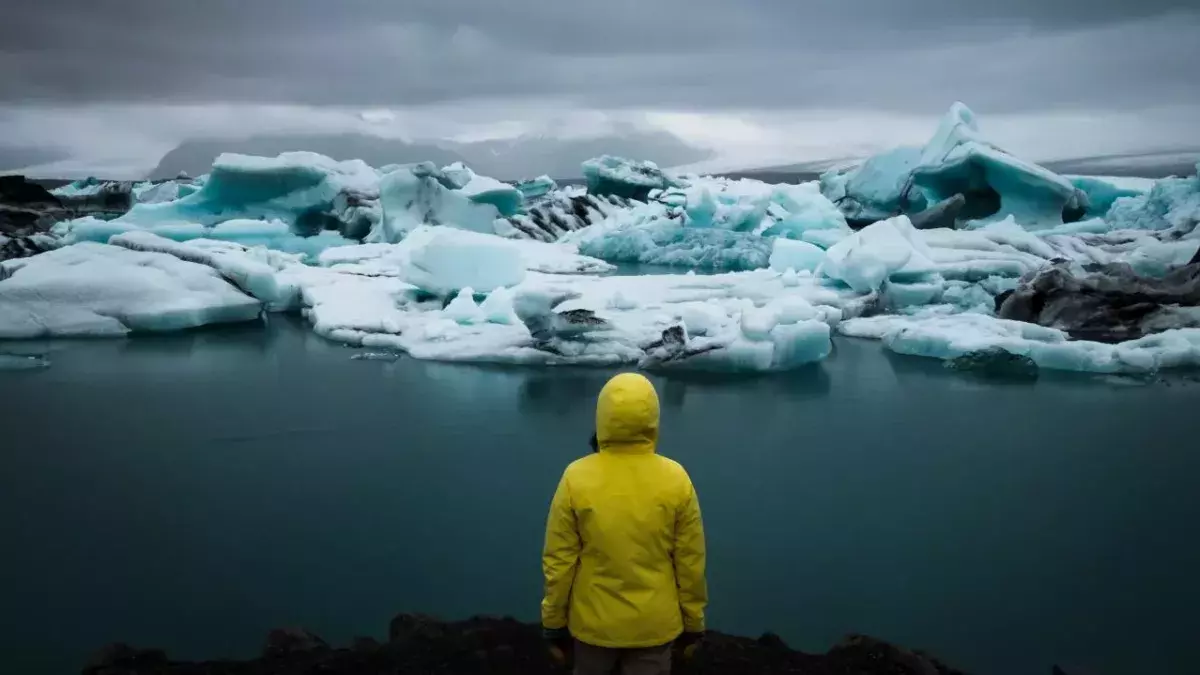 Eine Person mit gelber Regenjacke steht in Jökulsárlón, Island