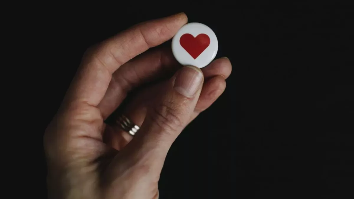 Eine Hand hält ein Herz-Button nach oben