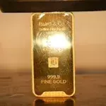 Ein Mann zerquetscht einen Goldbarren mit einer hydraulischen Presse