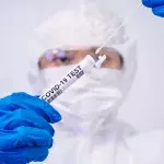 Ein Mediziner mit Schutzkleidung hält einen Corona-Test in den Händen
