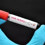 Eine Hand in Gummihandschuh hält eine positive Blutprobe mit Delta-Variante von COVID-19 