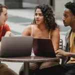 Drei junge Menschen sitzen mit dem Laptop an einem runden Tisch
