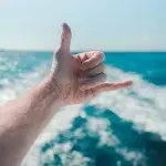 Ein Mann macht den Shaka-Gruß mit seiner linken Hand auf dem Ozean