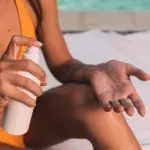Eine Frau im gelben Bikini sprüht sich mit Sonnenschutz ein