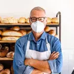Mann, der in einer Bäckerei arbeitet und eine Gesichtsmaske trägt, um das Corona-Virus zu vermeiden