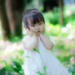 Ein kleines Mädchen in weißem Kleid auf einer Wiese in China