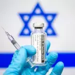 Eine Hand mit Impfstoff vor israelischer Flagge