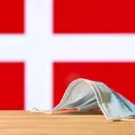 Eine medizinische Maske liegt auf dem Tisch vor dem Hintergrund der Flagge von Dänemark