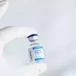 Hand mit Gummihandschuh hält ein Covid-19-Vakzin
