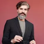 Ein Mann mit grauer Haarpartie posiert vor einem roten Hintergrund