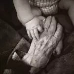 Eine faltige Hand umfasst die Hand eines Babys