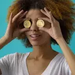 Eine Frau hält sich zwei Bitcoin-Münzen vor die Augen
