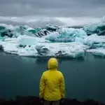 Eine Person mit gelber Regenjacke steht in Jökulsárlón, Island