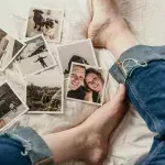 Polaroids liegen verstreut vor den Beinen einer Person auf einem Bett