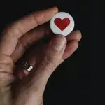 Eine Hand hält ein Herz-Button nach oben