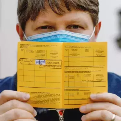 Ein Mann mit Mund-Nasen-Schutz hält einen gelben Impfpass in den Händen