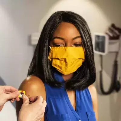 Eine schwarze Frau mit gelber Maske bekommt nach einer Impfung einen Pflaster aufgeklebt
