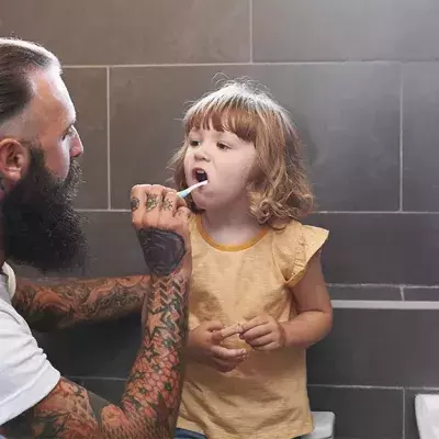 Tätowierter Vater putzt seiner Tochter die Zähne