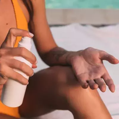 Eine Frau im gelben Bikini sprüht sich mit Sonnenschutz ein