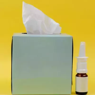 Eine Packung Taschentücher und ein Nasenspray vor gelbem Hintergrund