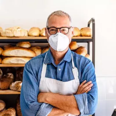 Mann, der in einer Bäckerei arbeitet und eine Gesichtsmaske trägt, um das Corona-Virus zu vermeiden