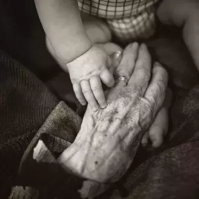 Eine faltige Hand umfasst die Hand eines Babys