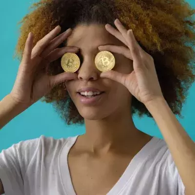 Eine Frau hält sich zwei Bitcoin-Münzen vor die Augen