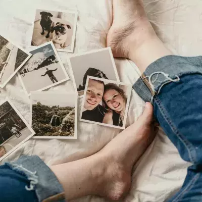 Polaroids liegen verstreut vor den Beinen einer Person auf einem Bett