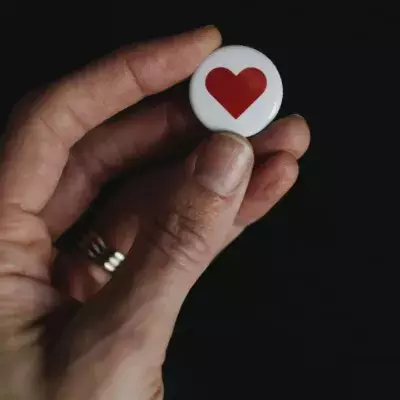 Eine Hand hält ein Herz-Button nach oben