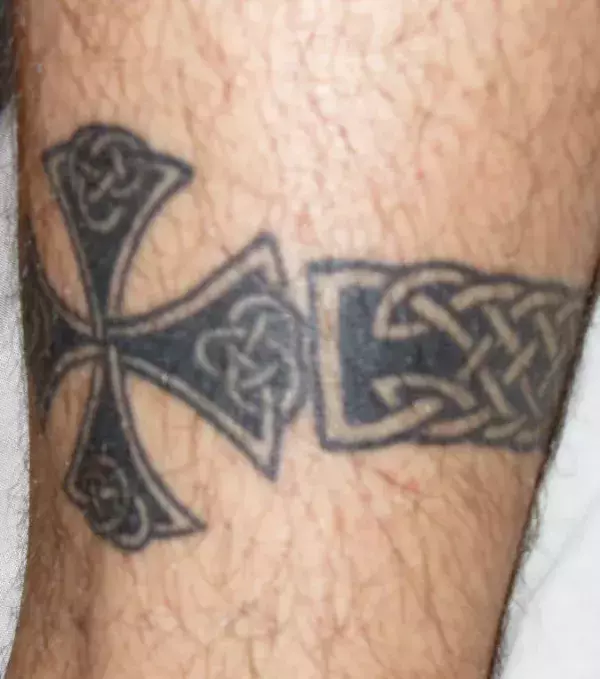 Auf der Wade eines Mannes: ein Tattoo mit einem keltischen Kreuz