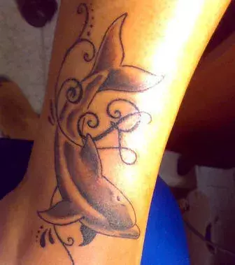 Feminines Tattoo des Buchstaben R mit Delfinen auf der Wade