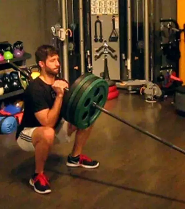 Squats mit Hantelstange: Macht einen Squat und haltet dabei eine Hantelstange mit beiden Händen fest, steht anschließend auf und drückt die Stange nach oben.