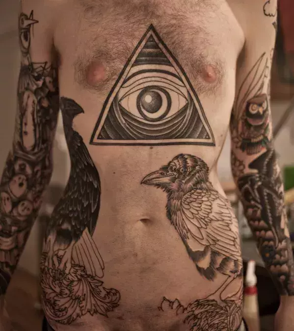 Tattoo allsehendes Auge und Rabe auf dem Oberkörper eines Mannes