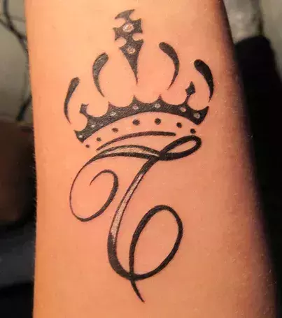 Tattoo des Buchstaben T mit Krone auf dem Unterarm