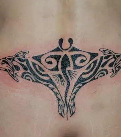 Tattoos für Frauen: Tribal Tattoo mit Delfinen und Rochen auf dem Steißbein einer Frau
